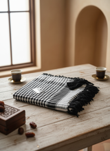 Black and white checkered keffiyeh on a wooden table with coffee cups and cookies.